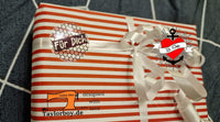 Ein liebevoll verpacktes Geschenk mit einem Button-Aufkleber "Für Dich" und einem weißen Schleifenband, das die kreative Note des Designs von easy-sticks zeigt. Die Geschenkverpackung ist mit roten und weißen Streifen gestaltet, was das Farbschema harmonisch ergänzt. Ideal für persönliche Geschenke.
