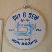 Handgefertigter Wandbehang mit dem 'Cut & Sew' Motiv in blauer Schrift auf hellem Hintergrund. Inspirierendes Design von easy-sticks für kreative Bastelarbeiten.