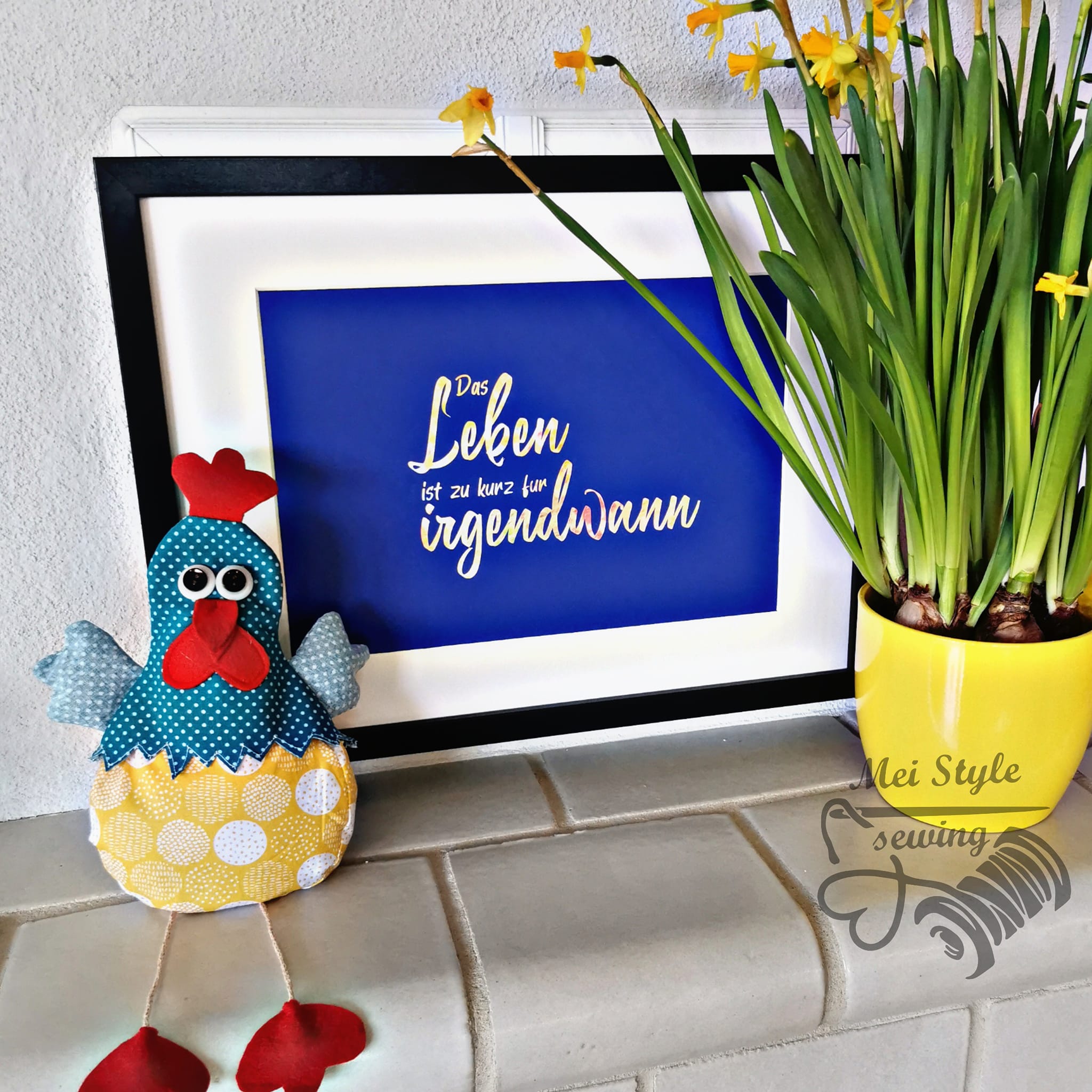 Kreatives Dekoobjekt mit der Plotterdatei "Das Leben ist zu kurz für irgendwann" von easy-sticks, das einen bunten Stoffhuhn und eine gelbe Blumentopf mit frischen Blumen zeigt.