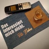 Das interessiert mich nicht. Die Bohne Plotterdatei von easy-sticks, dargestellt auf einem Tisch mit einem Telefon, einem Glas und einem Platzdeckchen aus Stoff, das kreativ gestaltet ist.