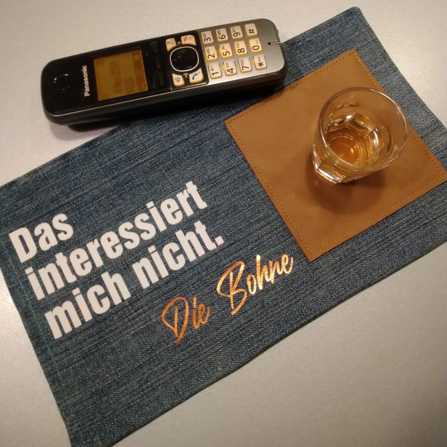 Das interessiert mich nicht. Die Bohne Plotterdatei von easy-sticks, dargestellt auf einem Tisch mit einem Telefon, einem Glas und einem Platzdeckchen aus Stoff, das kreativ gestaltet ist.