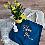 Praktische Tragetasche mit der Aufschrift "Die Welt ist schön, weil Du drauf bist" von easy-sticks, umgeben von fröhlichen gelben Blumen und einem dekorativen Hasen.