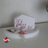 Ein dekorativer Tischaufsteller aus Holz mit dem Slogan "Die beste Zeit ist jetzt" von easy-sticks, umgeben von floralen Akzenten, ideal für jeden Raum.