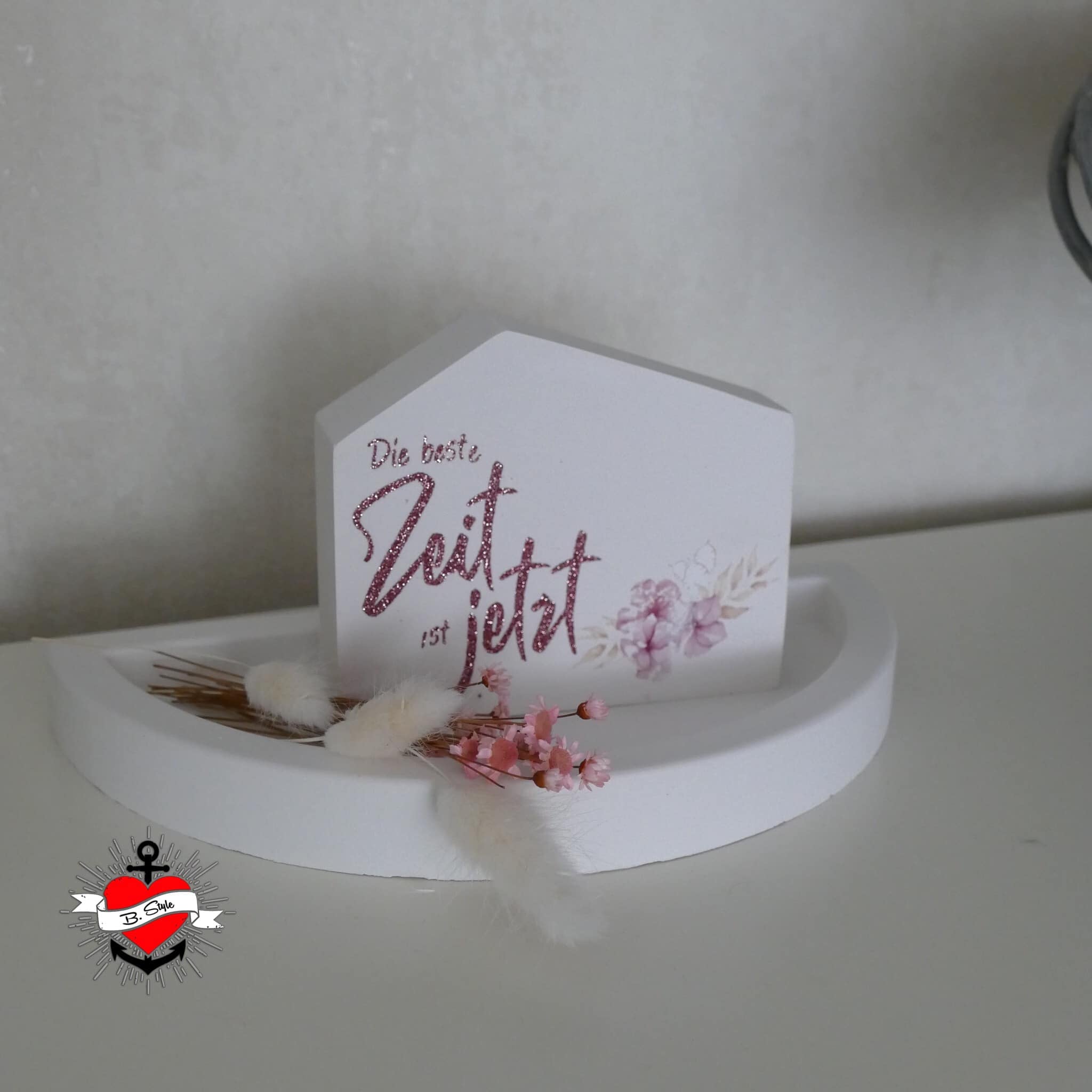 Ein dekorativer Tischaufsteller aus Holz mit dem Slogan "Die beste Zeit ist jetzt" von easy-sticks, umgeben von floralen Akzenten, ideal für jeden Raum.