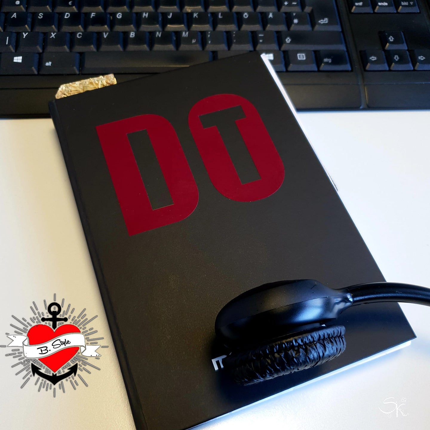 Inspirierende Aufnahme eines Notizbuchs mit der "DO IT" Plotterdatei von easy-sticks, auf einem Schreibtisch, neben einem Kopfhörer, bereit für kreative Projekte und individuelle Designs.