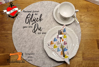 Kreative Tischdekoration mit dem Spruch 'Manchmal flüstert das Glück ganz leise: Du bist dran' als Plotterdatei von easy-sticks. Die Datei wird auf einem runden Untersetzer präsentiert, einschließlich Tellern und buntem Stoffserviette, ideal für persönliche Bastelprojekte.