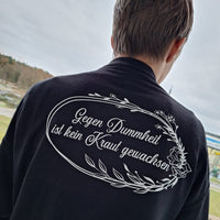 Ausdrucksstarke Textilgestaltung mit dem Spruch 'Gegen Dummheit ist kein Kraut gewachsen' auf einem schwarzen Shirt, kreiert von easy-sticks.