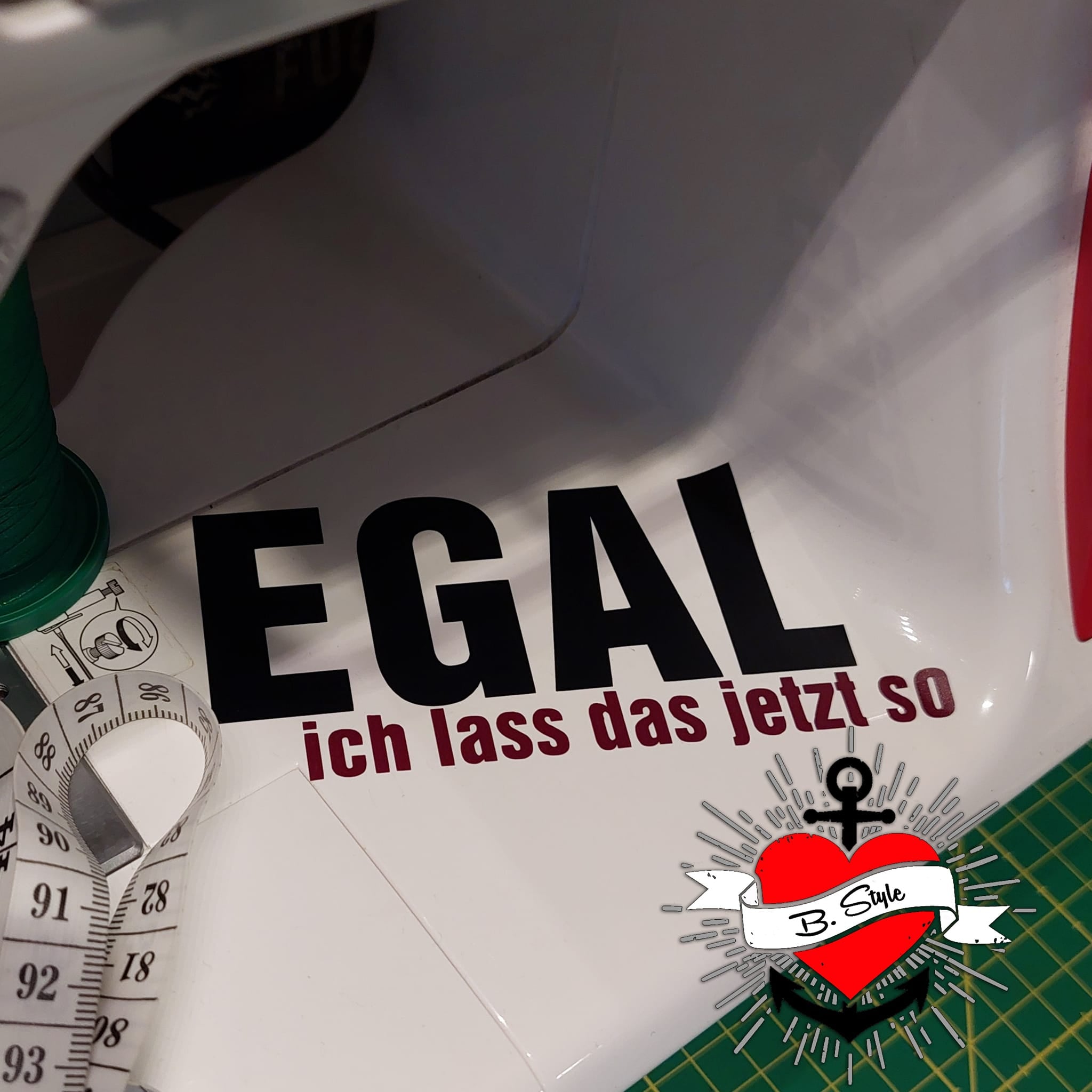 Nahtod e im kreativen Schaffensprozess: Auf einer Nähmaschine prangt die Aufschrift 'EGAL ich lass das jetzt so', entworfen von easy-sticks - eine perfekte Plotterdatei für DIY-Projekte.