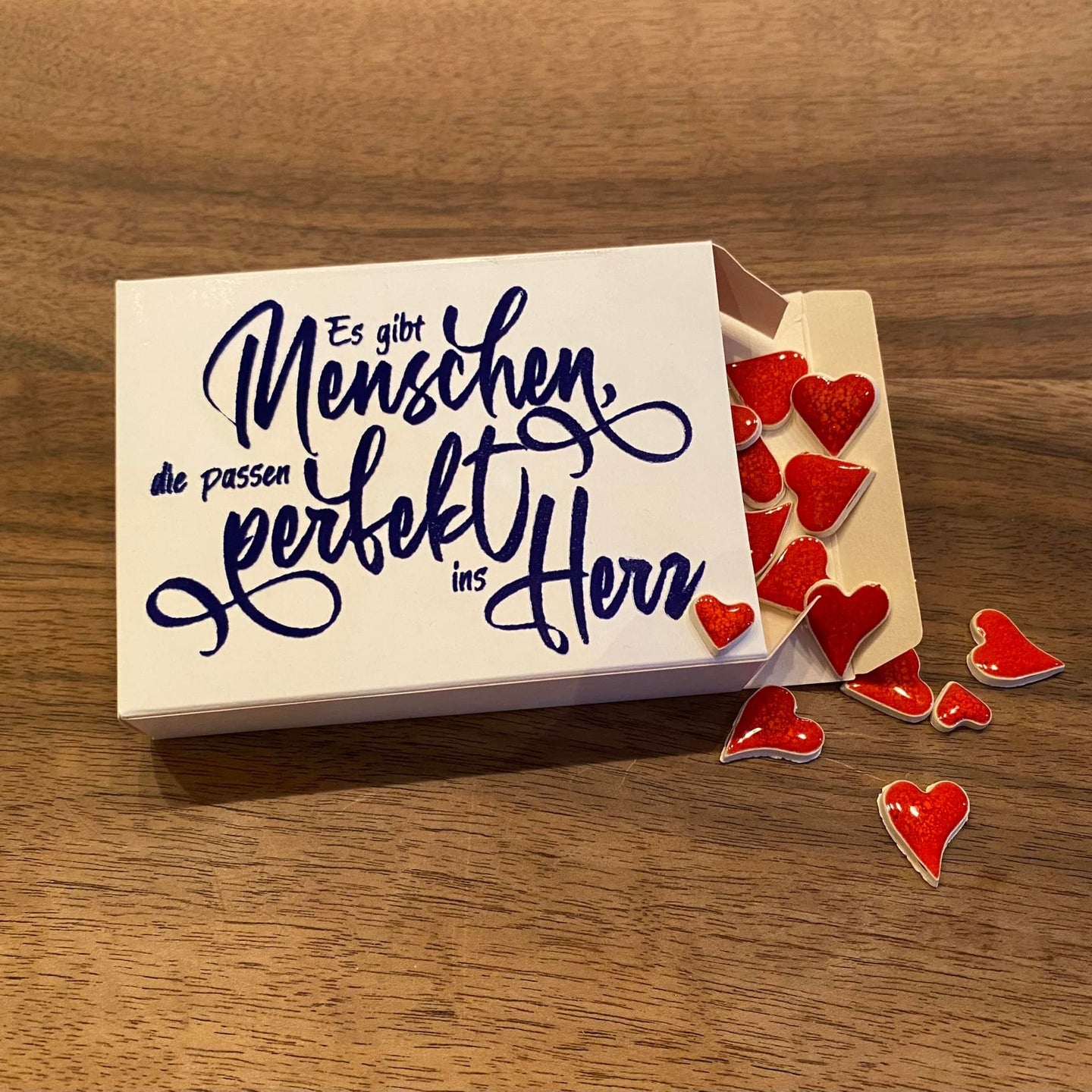 Die Plotterdatei "Es gibt Menschen die passen perfekt ins Herz" von easy-sticks, dargestellt auf einer Geschenkbox mit Herzen. Perfekt für individuelle Bastelprojekte.