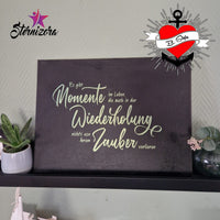 Wandbild mit dem Spruch "Es gibt Momente im Leben die auch in der Wiederholung nichts von ihrem Zauber verlieren" von easy-sticks, präsentiert auf einem Regal neben einer dekorativen Pflanze.