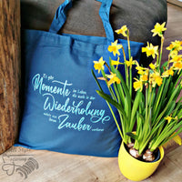 Tasche mit dem Schriftzug "Es gibt Momente im Leben die auch in der Wiederholung nichts von ihrem Zauber verlieren" von easy-sticks, begleitet von gelben Blumen in einem Topf, ideal für kreative DIY-Projekte.