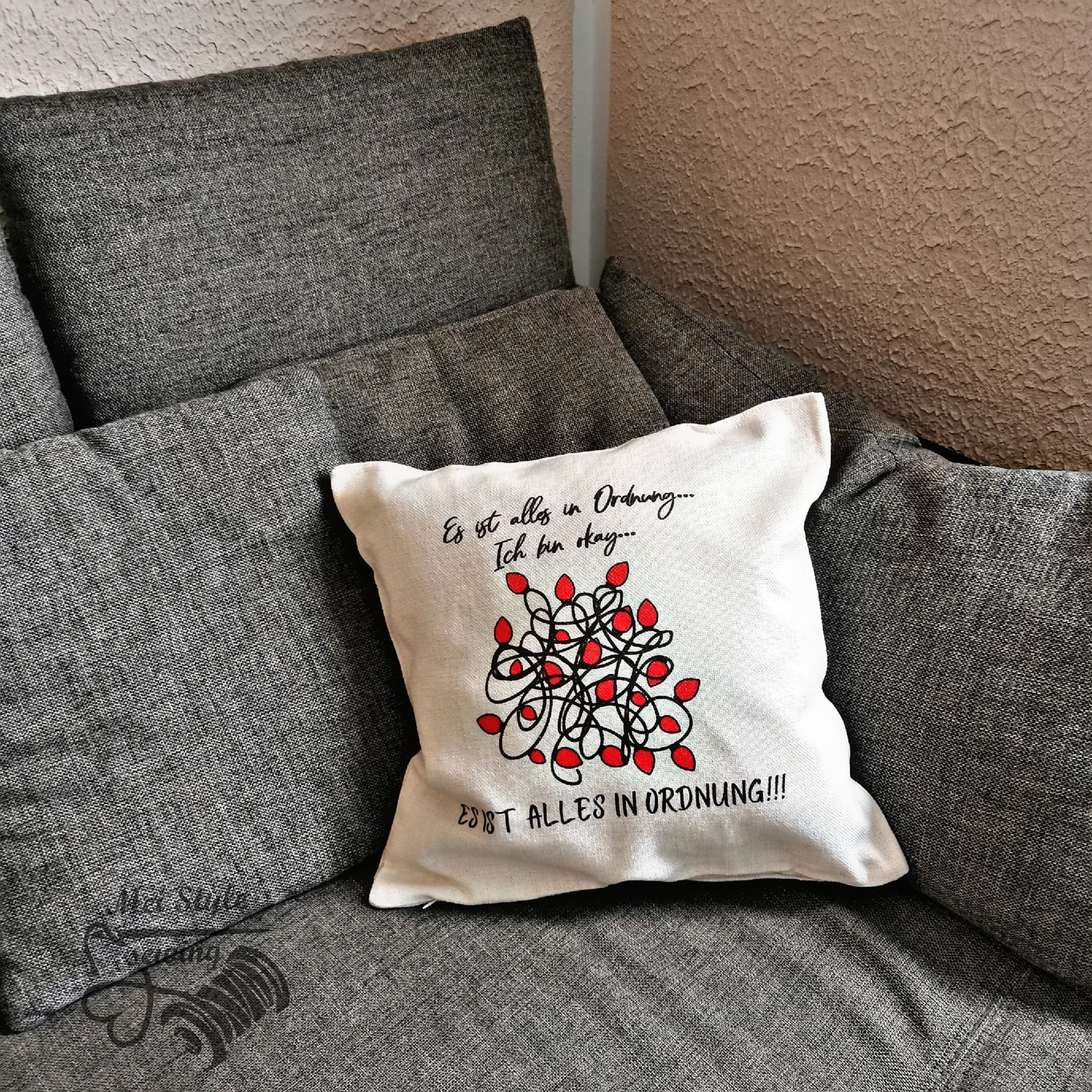 Dekoratives Kissen mit dem Aufdruck "Es ist alles in Ordnung...Ich bin ok...ES IST ALLES IN ORDNUNG" von easy-sticks, auf einem grauen Sofa platziert, perfekt für kreative DIY-Projekte.
