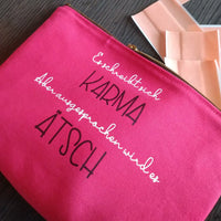 Ein pinker Kosmetiktäschchen mit dem Motiv "Es schreibt sich Karma Aber ausgesprochen wird es Ätsch" von easy-sticks, ideal für kreative DIY Projekte.