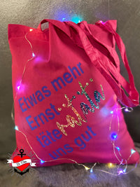 Eine pinke Tragetasche mit dem Druck "Etwas mehr Ernst..täteratata uns gut" von easy-sticks, verziert mit Lichtern, perfekt für kreative DIY-Ideen der Plotterdatei.
