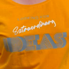 Frau trägt ein leuchtend orangefarbenes T-Shirt mit dem Aufdruck "Looking for extraordinary Ideas" von easy-sticks, perfekt für kreative Projekte.
