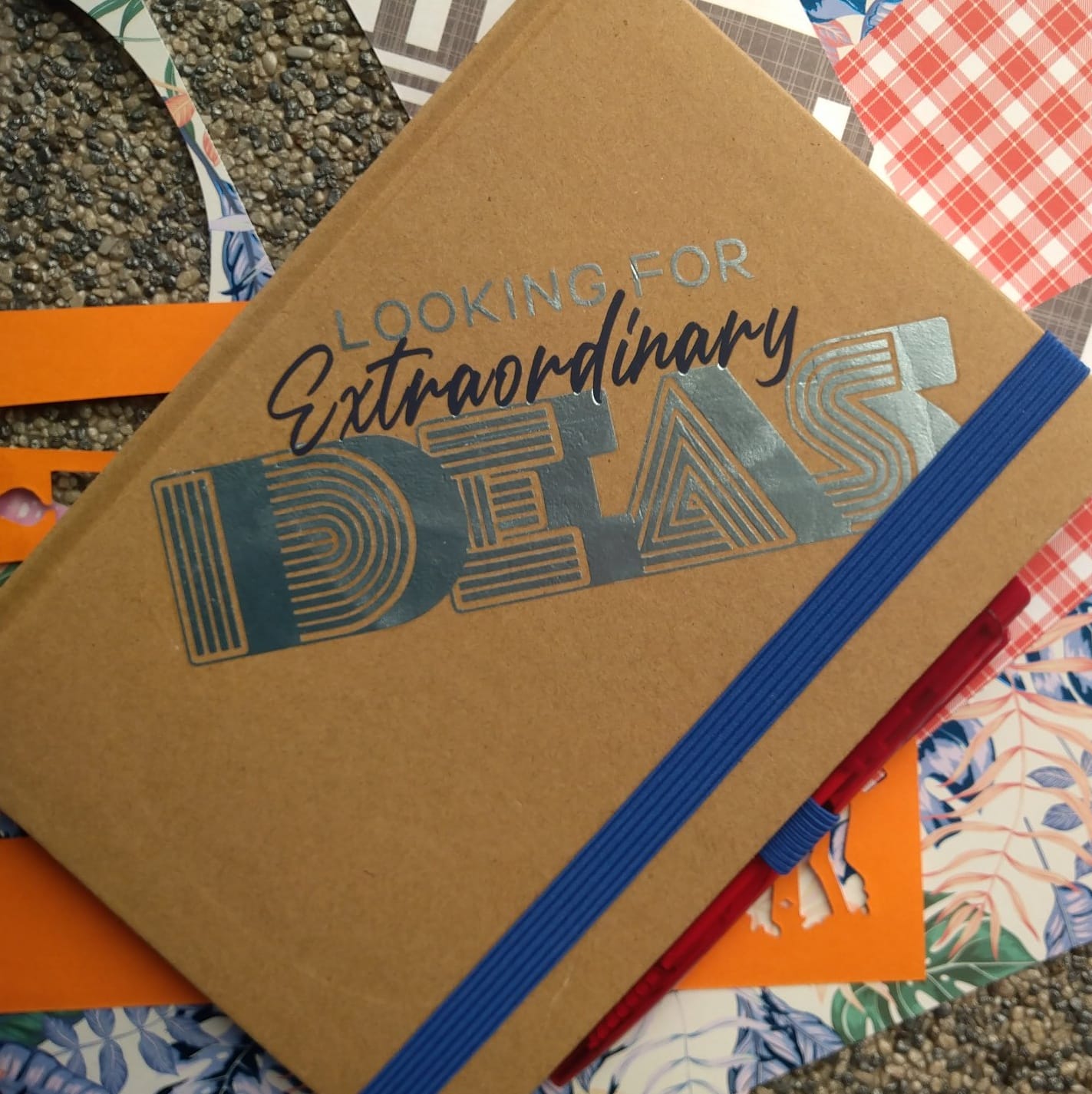 Braunes Notizbuch mit dem Druck "Looking for extraordinary Ideas" von easy-sticks, umgeben von bunten Bastelmaterialien für kreative Inspiration.