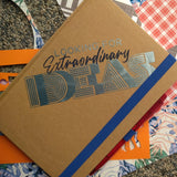 Braunes Notizbuch mit dem Druck "Looking for extraordinary Ideas" von easy-sticks, umgeben von bunten Bastelmaterialien für kreative Inspiration.