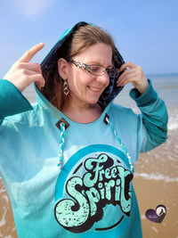 Frau am Strand trägt einen Hoodie mit dem auffälligen Aufdruck 'Free Spirit', erhältlich als Plotterdatei von easy-sticks.