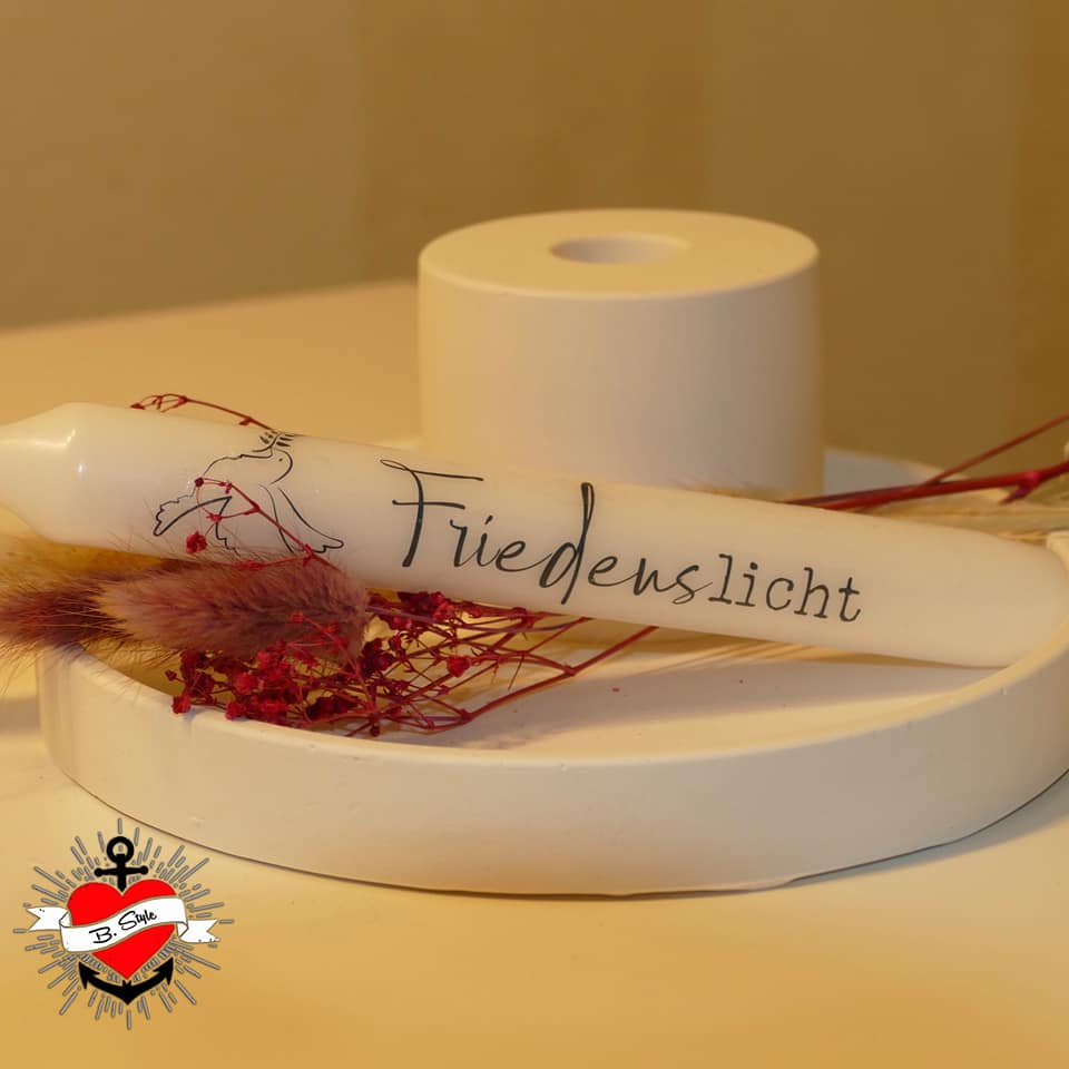 Eine friedliche Kerze mit der Aufschrift 'Friedenslicht' auf einem weißen Kerzenhalter, geschmückt mit Trockenblumen. Entdecke die Möglichkeiten der Kreativität mit der Friedenskerze PDF Datei und Plotterdatei von easy-sticks.