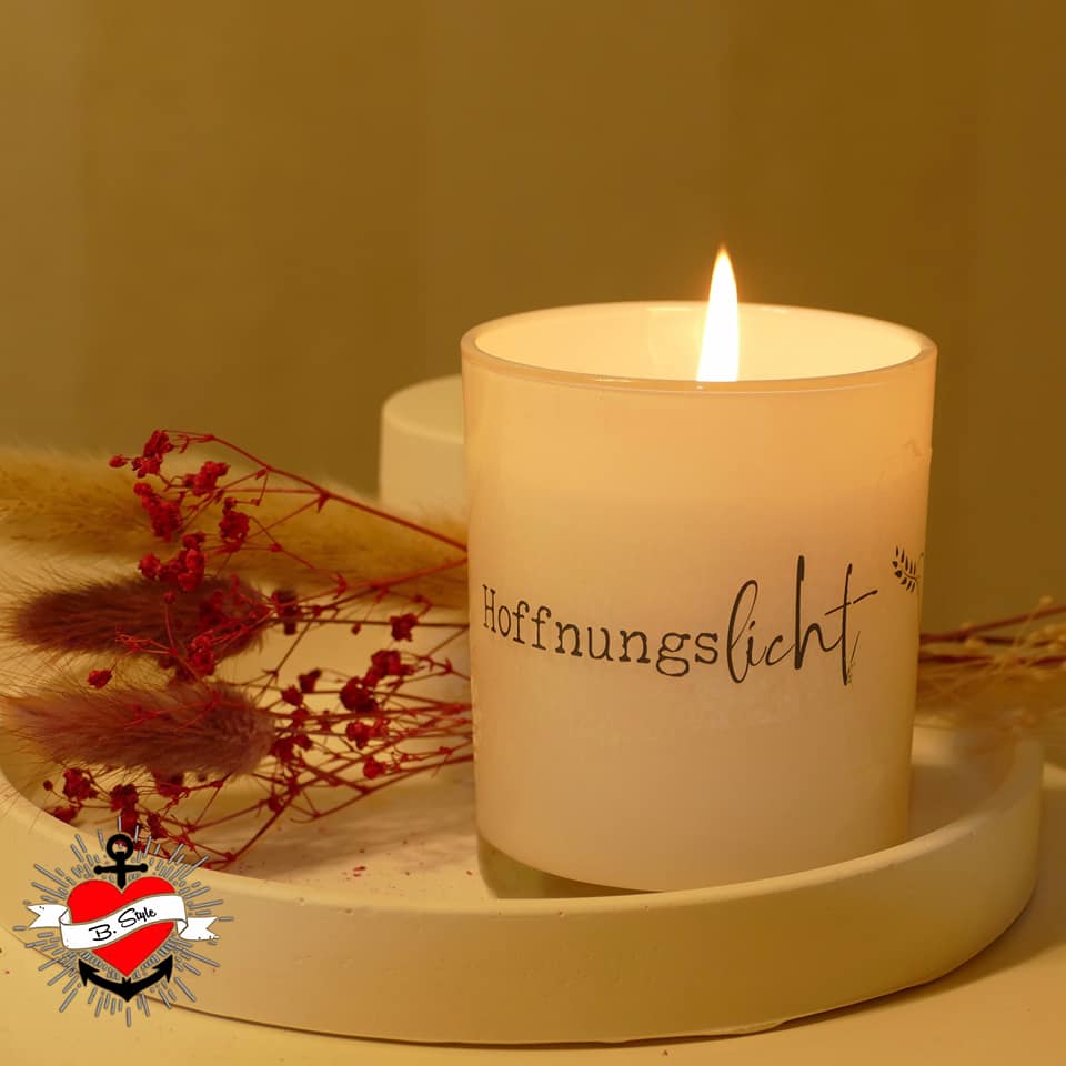 Eine brennende Friedenskerze 'Hoffnungslicht' in einem stilvollen Glasbehälter, umgeben von feinen floralen Elementen, die eine warme Atmosphäre schaffen. Erstelle einzigartige Designs mit der Friedenskerze PDF Datei und Plotterdatei von easy-sticks.