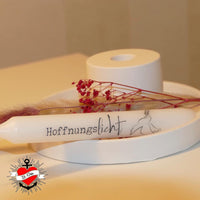 Eine elegante Friedenskerze 'Hoffnungslicht', platziert auf einem minimalistischen, weißen Untergrund, umgeben von dekorativen Zweigen und floralen Akzenten. Lass deiner Kreativität mit der Friedenskerze PDF Datei und Plotterdatei von easy-sticks freien Lauf.