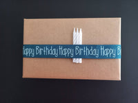Kreativ verpacktes Geburtstagsgeschenk mit einer blauen Schleife, die "Happy Birthday" aufgedruckt hat, ideal für DIY-Projekte mit der Geburtstagsgrüße Datei zum Plotten und Drucken von easy-sticks.