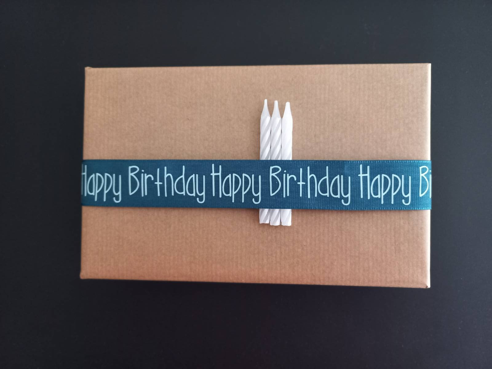 Kreativ verpacktes Geburtstagsgeschenk mit einer blauen Schleife, die "Happy Birthday" aufgedruckt hat, ideal für DIY-Projekte mit der Geburtstagsgrüße Datei zum Plotten und Drucken von easy-sticks.
