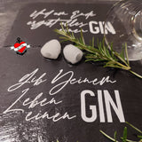 Ein stilvolles Set mit einer GIN Trinksprüche Plotterdatei von easy-sticks, präsentiert auf einer Schieferplatte. Im Vordergrund stehen zwei Eiswürfel und ein Rosmarinzweig, während der Spruch 'Gib Deinem Leben einen GIN' in geschwungener Schrift zu sehen ist. Ein elegantes Glaskelch rundet das Bild ab und verleiht dem Gesamtbild einen Hauch von Genuss.