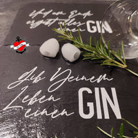 Ein stilvolles Set mit einer GIN Trinksprüche Plotterdatei von easy-sticks, präsentiert auf einer Schieferplatte. Im Vordergrund stehen zwei Eiswürfel und ein Rosmarinzweig, während der Spruch 'Gib Deinem Leben einen GIN' in geschwungener Schrift zu sehen ist. Ein elegantes Glaskelch rundet das Bild ab und verleiht dem Gesamtbild einen Hauch von Genuss.