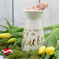 Elegante Vase mit der inschriftlichen Botschaft 'Ab hier beginnt das Glück', gestaltet von easy-sticks. Die goldene Schrift auf dem weißen Keramikgefäß macht es zu einem stilvollen Dekorationsstück.