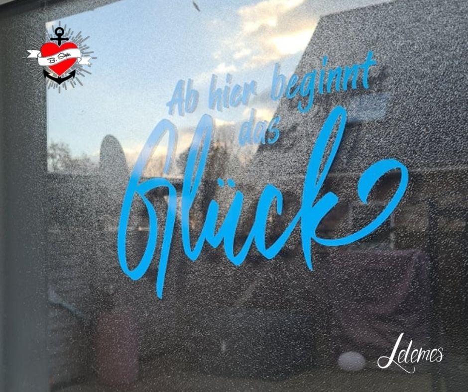 Fensterdekoration mit dem Text 'Ab hier beginnt das Glück' in leuchtendem Blau, erstellt von easy-sticks. Der klare Hintergrund lässt die Schrift lebendig erscheinen und eignet sich perfekt für kreative Projekte.