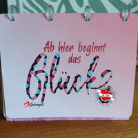 Illustration eines inspirierenden Notizbuchs von easy-sticks mit buntem Design und dem Titel 'Ab hier beginnt das Glück', das Kreativität und Glück symbolisiert.