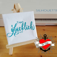 Kreatives Projekt mit der Plotterdatei "Einfach Glücklich sein" von easy-sticks, präsentiert auf einer kleinen Staffelei. Das Design zeigt den inspirierenden Schriftzug "glücklich sein" in stilvollem Türkis und erzeugt eine positive Atmosphäre.