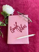 Elegantes pinkes Notizbuch mit dem Schriftzug 'Good Vibes' aus der Plotterdatei von easy-sticks, dekoriert mit einer Blume und Brille.