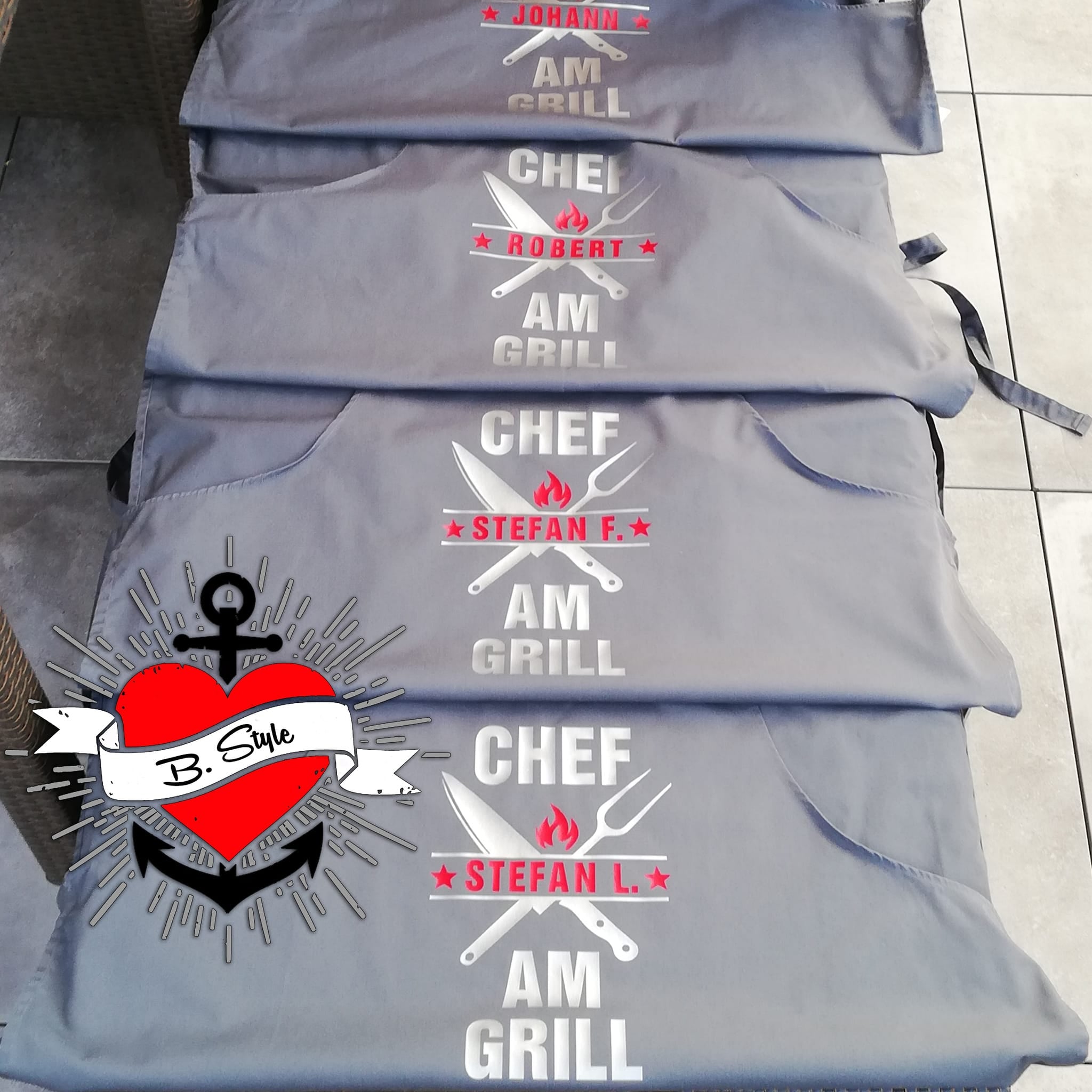 Stylische Grillköche Schürzen mit dem Aufdruck "CHEF AM GRILL". Fünf personalisierte Schürzen von easy-sticks, perfekt für Grillpartys oder als Geschenk für Grillfans.