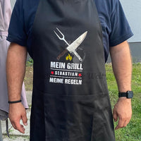 Ein elegantes schwarzes Grill-Schürze mit der Aufschrift "MEIN GRILL SEBASTIAN MEINE REGELN" und passenden Grillwerkzeugen, perfekt für kreative Grillprojekte von easy-sticks, basierend auf der "Grill Sprüche" Plotterdatei.
