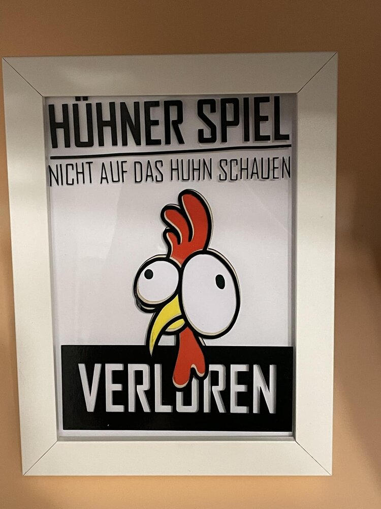 Kreative Darstellung des Hühner Spiels von easy-sticks, mit einem lustigen Hühner-Motiv und dem Text "Nicht auf das Huhn schauen - Verloren" in einem schicken weißen Rahmen.