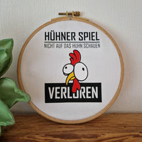 Originelles Stickbild des Hühner Spiels von easy-sticks, das ein charakteristisches Hühner-Motiv zeigt mit dem Spruch "Nicht auf das Huhn schauen - Verloren" in einem hübschen Holzrahmen.
