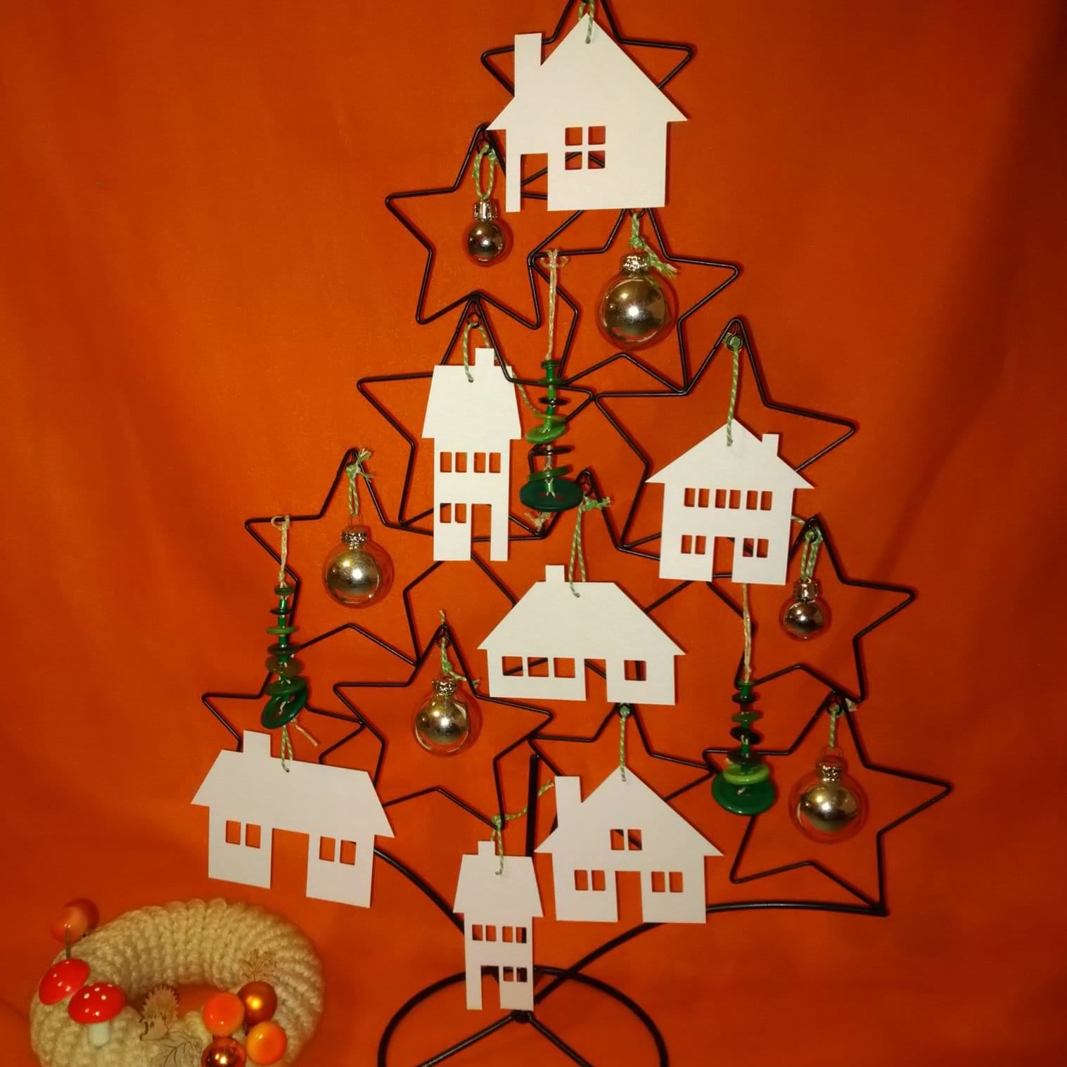 Ein dekorativer Weihnachtsbaum aus Draht mit weißen Häusersilhouetten von easy-sticks, die die "Häuser" Plotterdatei darstellen, umgeben von buntem Weihnachtsschmuck.