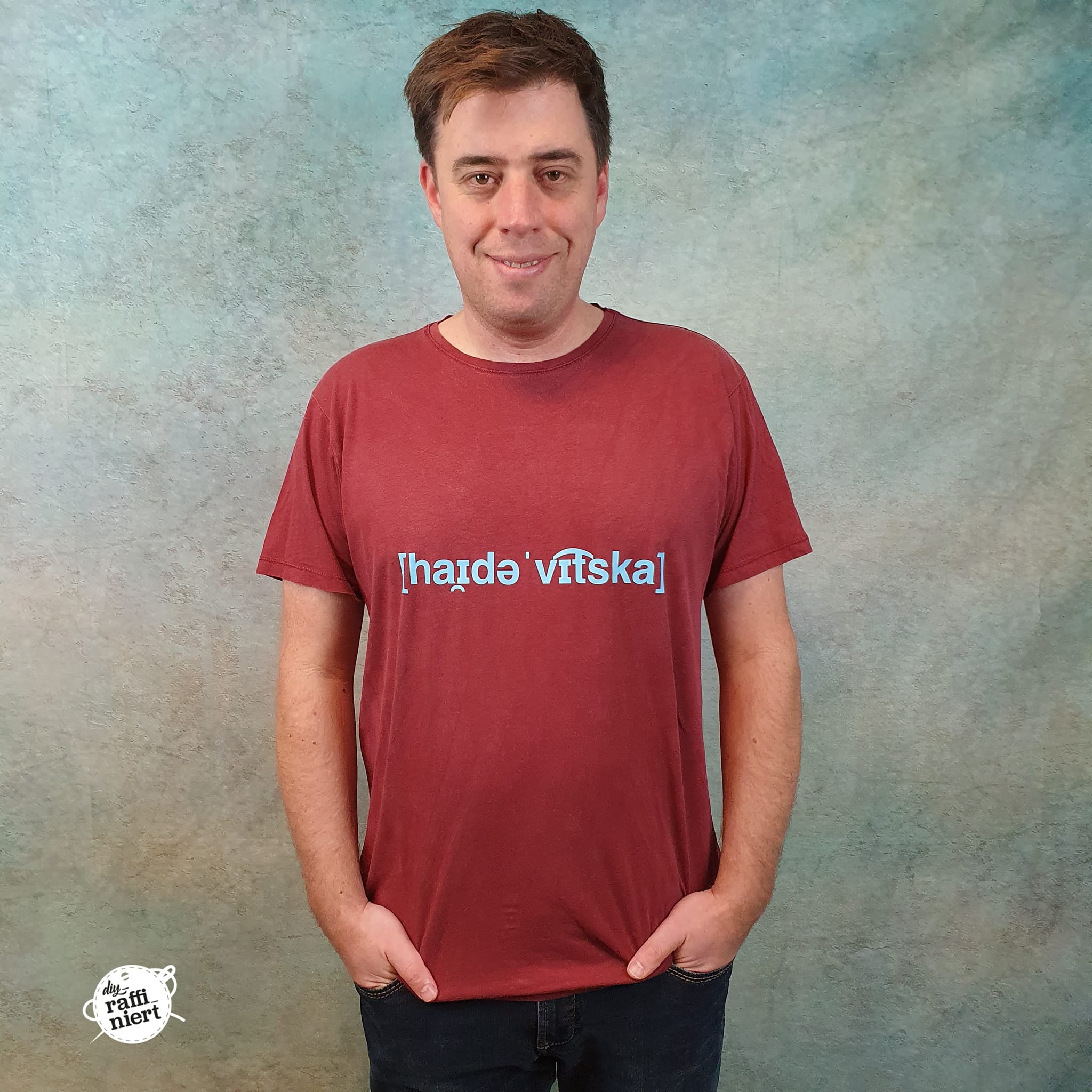 Ein Mann trägt ein rotes T-Shirt mit der Aufschrift '[hˈaɪdɘ vɪtska]' und präsentiert die 'Heidewitzka' Lautschrift Plotterdatei von easy-sticks.