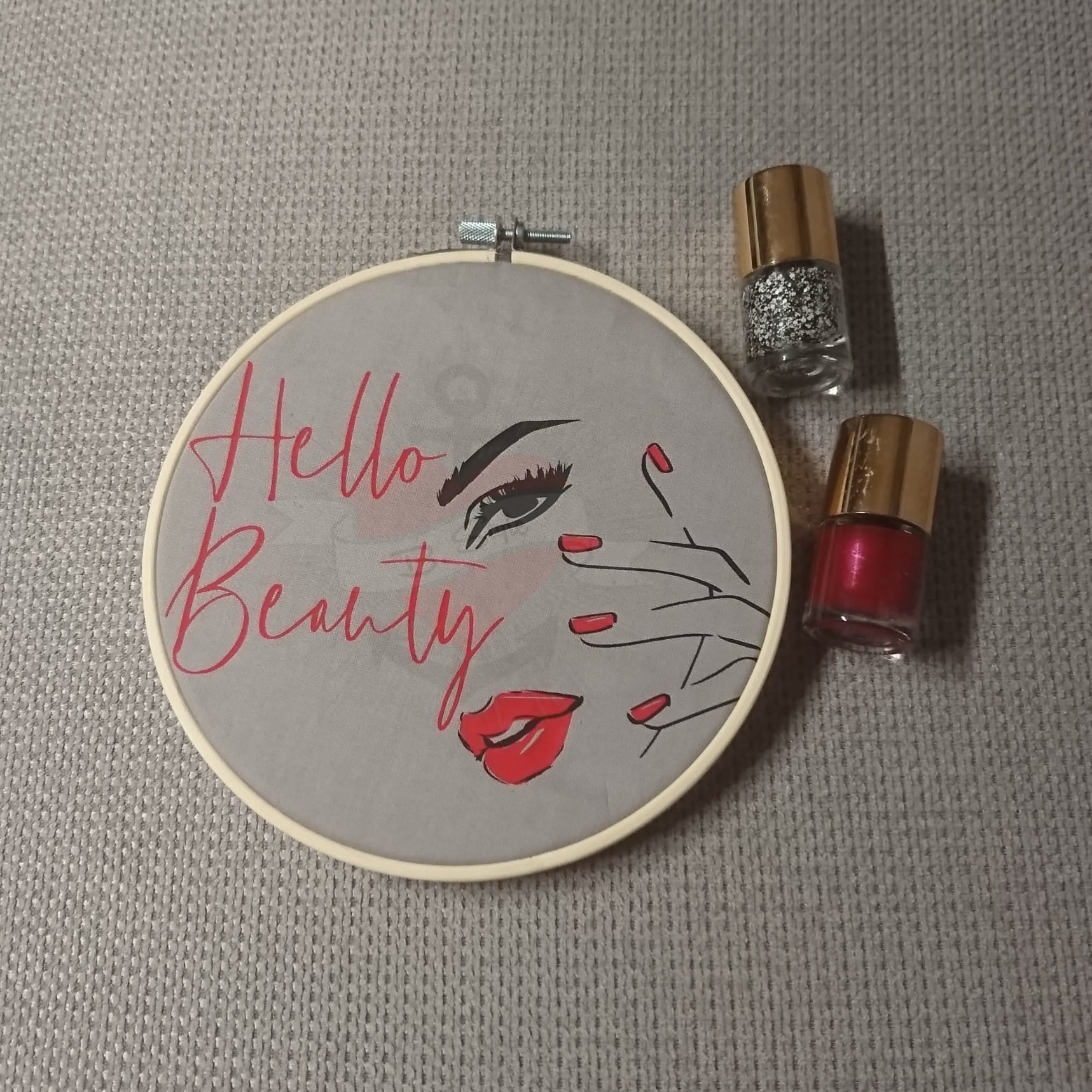 Stickrahmen mit dem Schriftzug "Hello Beauty" von easy-sticks, umgeben von Nagellackfläschchen, eine kreative Dekoration für dein Zuhause.