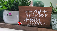 Dekoratives Holzschild mit der Plotterdatei "Lass immer ein wenig Platz in deinem Herzen für das Unvorstellbare" von easy-sticks, umgeben von Pflanzen.
