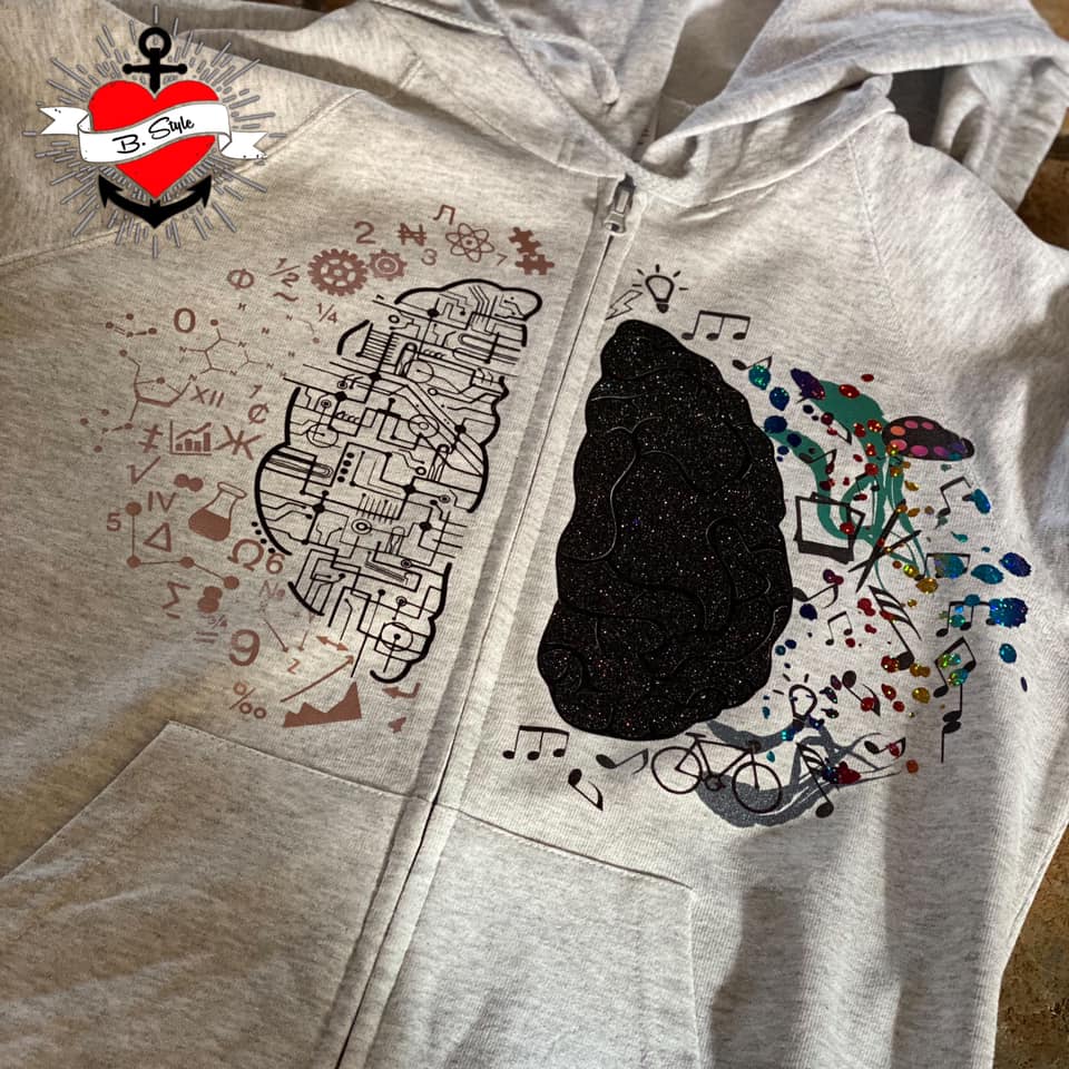 Graue Kapuzenjacke mit kreativer Grafik, die das Hirn in zwei Hälften darstellt: eine Seite technisch und analytisch, die andere kreativ und farbenfroh, von easy-sticks, basierend auf der Hirn Plotterdatei.