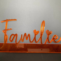 Detaillierte Aufnahme des orangefarbenen Acryl Aufstellers 'Familie' von Easy-Sticks, auf einem grauen Hintergrund, strahlt Eleganz aus.