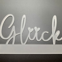 Transparenter Easy-Sticks Acryl Aufsteller 'Glück', vor einem dunklen Hintergrund, hebt sich durch das elegante Design ab, ideal für besondere Geschenkideen.
