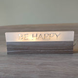 Acryl-Easy-Stick 'BE HAPPY' von Easy-Sticks, im Warmlicht leuchtend auf einem Holzuntergrund, perfektes Deko-Element.