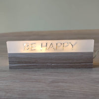 Acryl-Easy-Stick 'BE HAPPY' von Easy-Sticks, im Warmlicht leuchtend auf einem Holzuntergrund, perfektes Deko-Element.