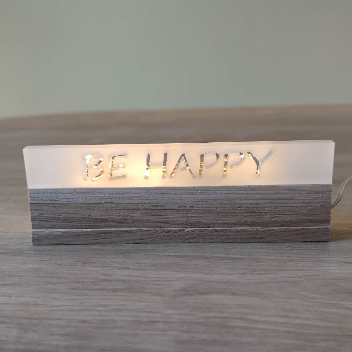 Acryl-Easy-Stick 'BE HAPPY' von Easy-Sticks, im Warmlicht leuchtend auf einem Holzuntergrund, perfektes Deko-Element.