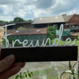 Handgehaltener Acrylschriftzug "Freunde" von Easy-Sticks, vor einer grünen Landschaft, perfekt für persönliche Geschenke und stilvolle Dekorationen.
