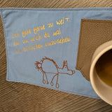 Elegante Plotterdatei von easy-sticks mit dem Spruch 'Ich gehe gerne zu weit. Nur um mich da mal ein bisschen umzusehen.' auf blauem Stoff neben einer Tasse.